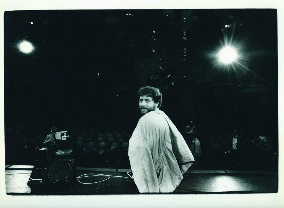Schwarzweißfoto von der Bühne aus: Harry Pepl blickt über die Schulter in die Kamera, dahinter ein leerer Saal, eine Fernsehkamera und Scheinwerfer.