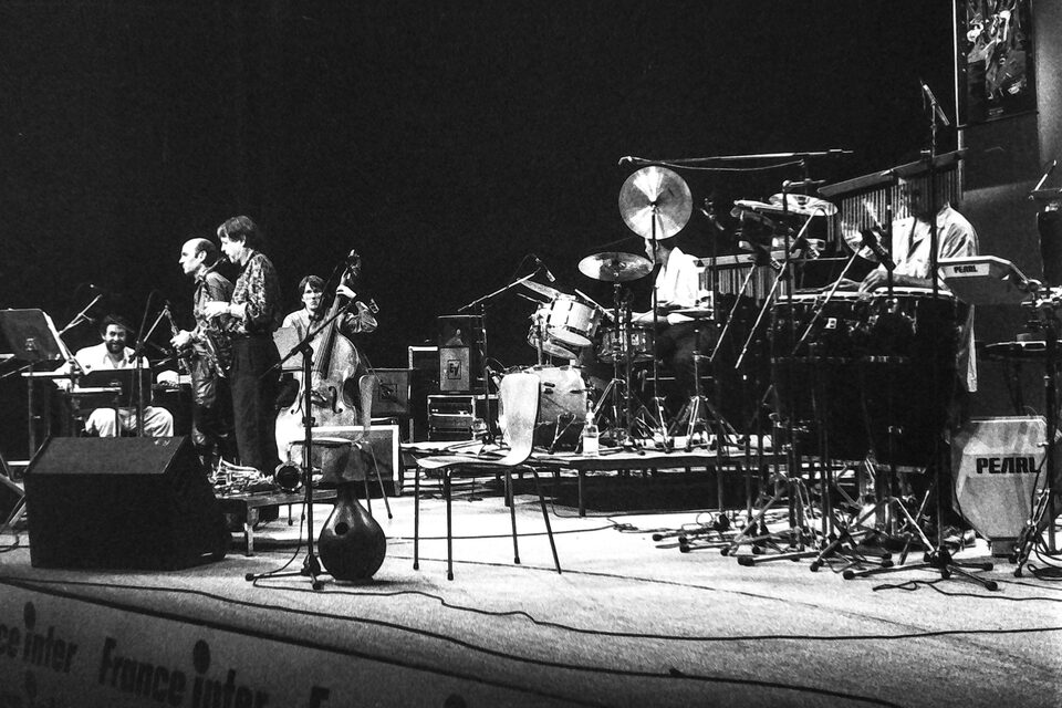 Die ganze Bühne beim Jazzfestival Amiens, Frankreich, Mai 1987: links Harry Pepl, zwei Saxophone und Kontrabass, rechts Schlagzeug und Percussion, vorn ein Banner von France Inter. Laut Besetzung von „Men's Land“ mit Michel Portal, Dave Liebman, Jean-François Jenny-Clark, Jack DeJohnette und Mino Cinelu.